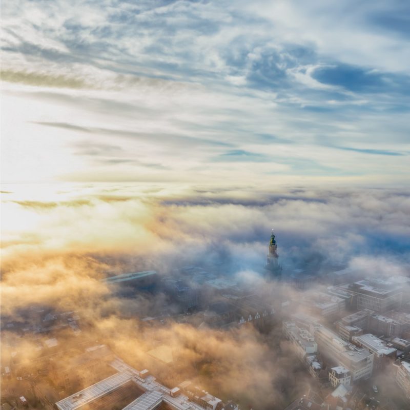 De Martinitoren in de mist terwijl de eerste zonnestralen door de wolken breken
