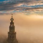 De top van de Martinitoren boven een dikke laag mist tijdens een gouden zonsopkomst